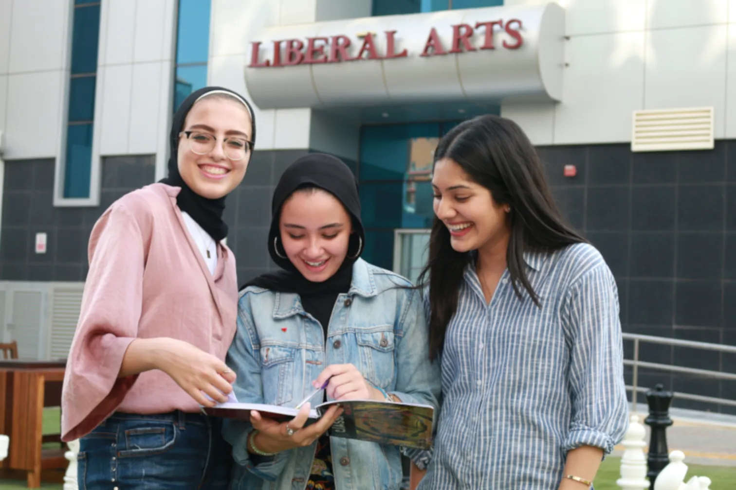 Three students from AUK's Liberal Arts department reading and discussing books together in a collaborative setting.