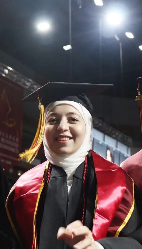 Three AUK graduates joyfully celebrate their achievements as graduates, wearing traditional caps and gowns after their ceremony.