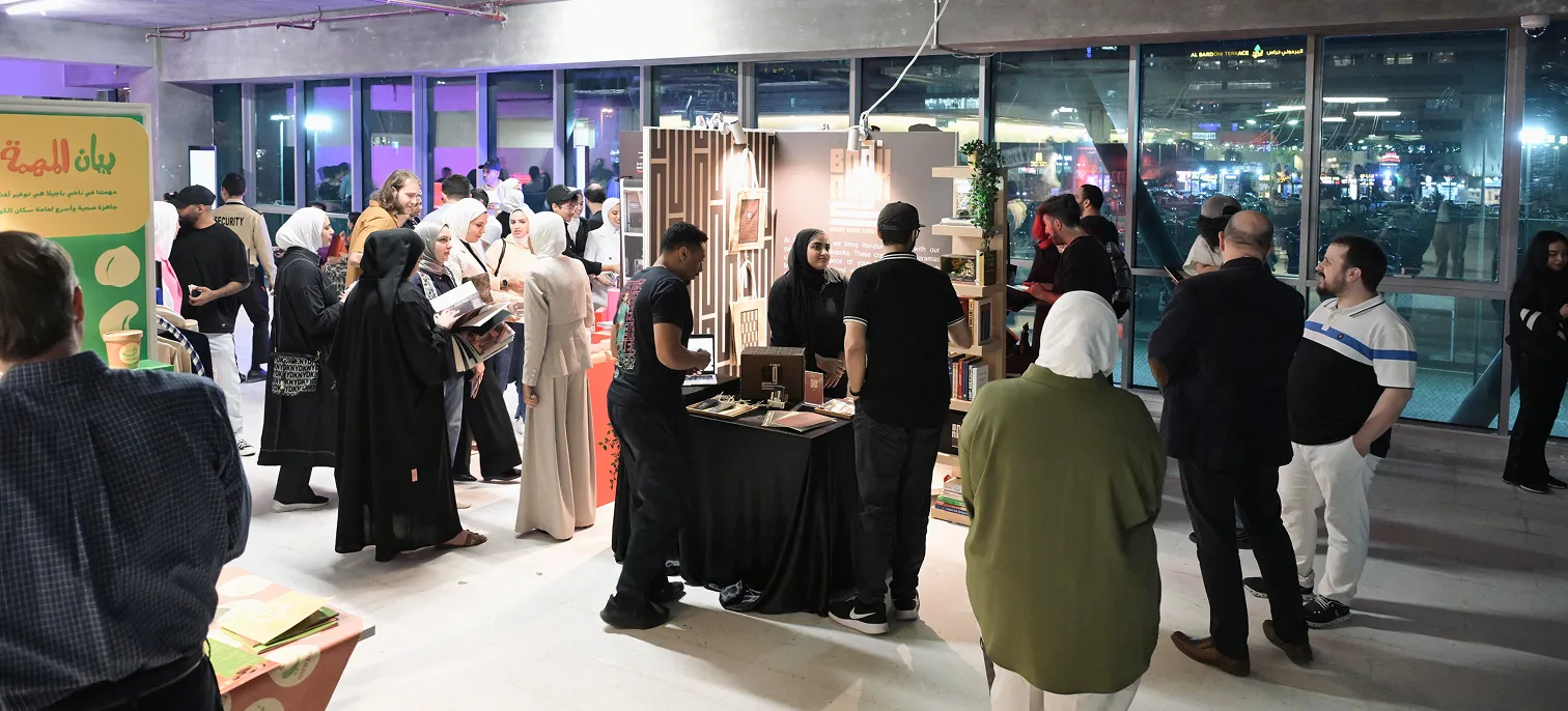 A vibrant event hosted by The American University Of Kuwait - AUK, with a group of people gathered and interacting.