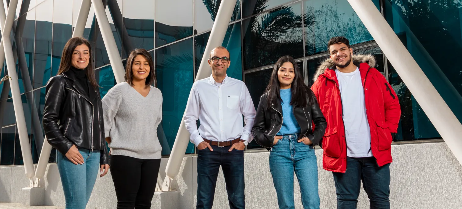 Four AUK students posing with a professor in front of the university, reflecting academic collaboration.