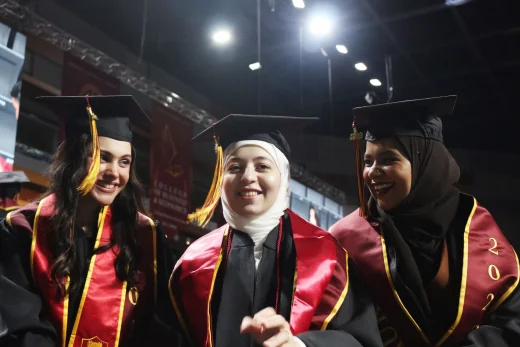 Three AUK graduates joyfully celebrate their achievements as graduates, wearing traditional caps and gowns after their ceremony.