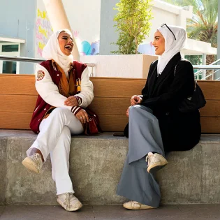Two AUK students sitting outside on campus, engaging in a thoughtful discussion.
