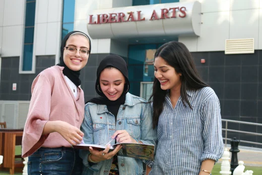 Three students from AUK's Liberal Arts department reading and discussing books together in a collaborative setting.
