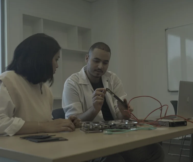 Two electrical engineering students at AUK engaged in an insightful discussion while working collaboratively in the lab.